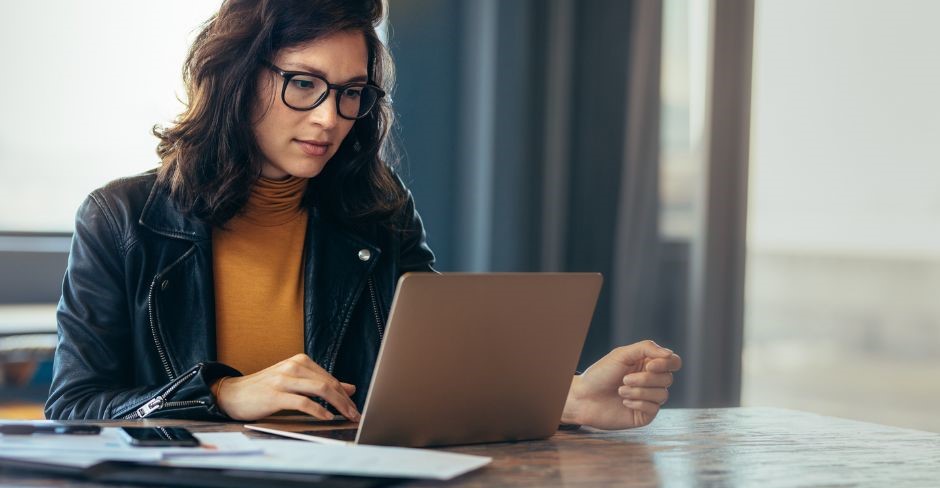 una donna seduta alla scrivania sta navigando nel suo pc portatile