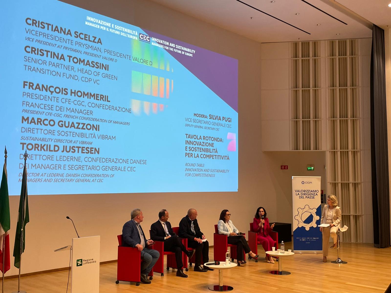 gruppo di sei persone sedute su un palco che dialogano tra loro in una sala congressi